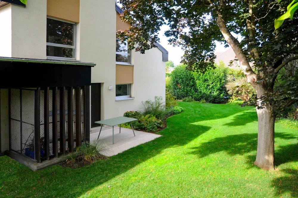 Terrasse en bois extérieure avec chaise design scandinave et table d'appoint, située dans un parc verdoyant aux arbres matures