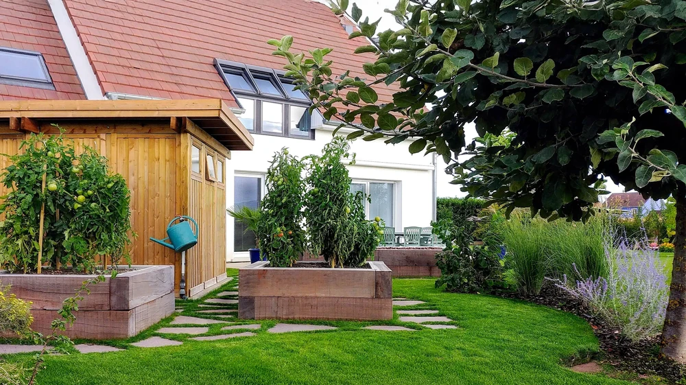 Terrasse couverte avec pergola en bois et colonnes blanches, mobilier de jardin en résine tressée avec coussins gris, donnant sur pelouse et aire de jeux
