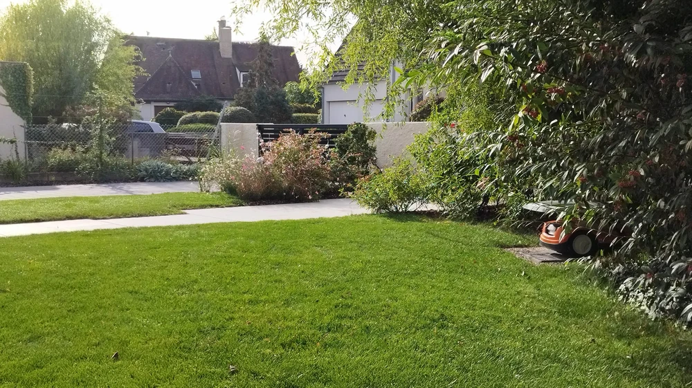 Terrasse extérieure en bois avec fauteuil suspendu en rotin, jardin paysager avec pelouse et végétation tropicale