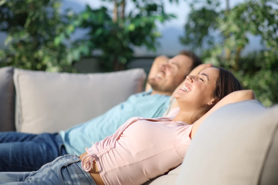 Un jardin ensoleillé avec des plantes en pot sur une terrasse en bois, une végétation luxuriante et une maison confortable en arrière-plan crée une atmosphère estivale paisible