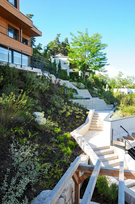 Terrasse extérieure contemporaine avec piscine illuminée en soirée, murs blancs éclairés par spots encastrés, maison moderne vitrée en arrière-plan, montagnes boisées
